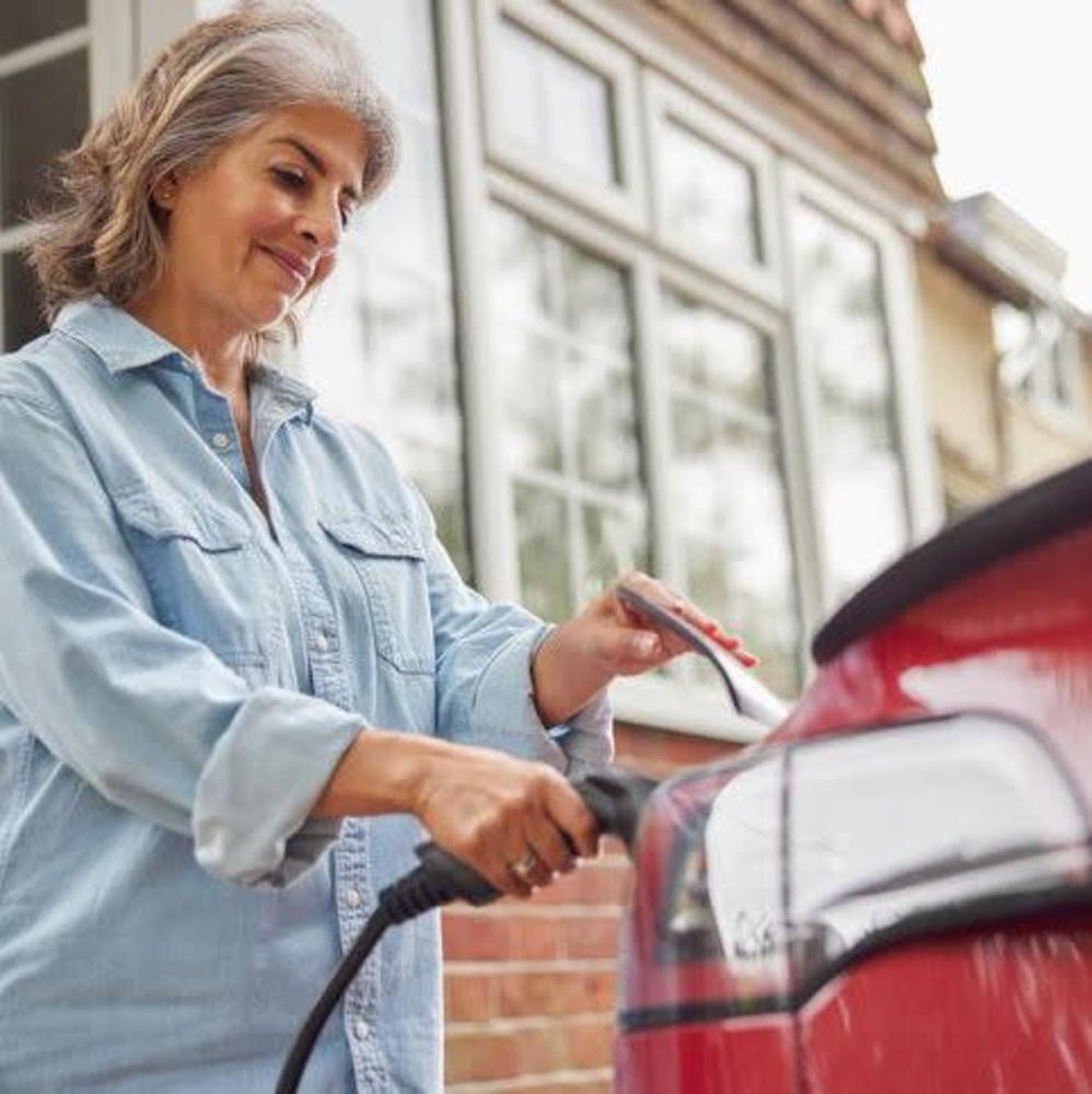 woman in blue shirt plugging in an EV